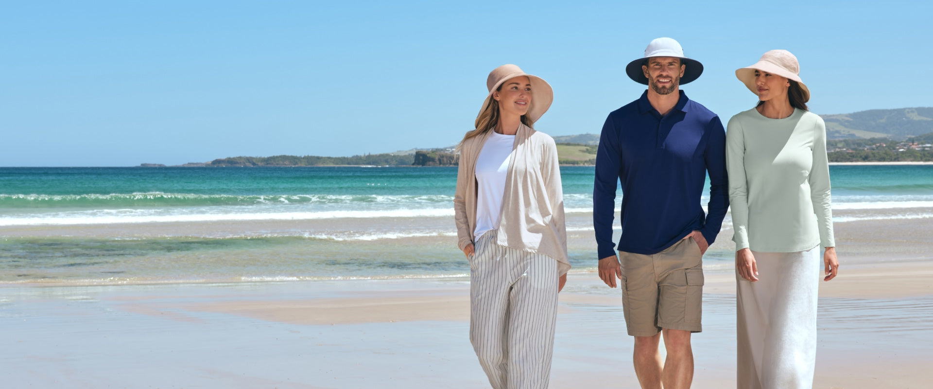 Three people standing on a beach wearing Solbari clothing with hats.