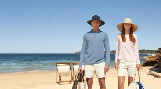 A woman and a man standing on the beach in sun hats and sun protective clothing.