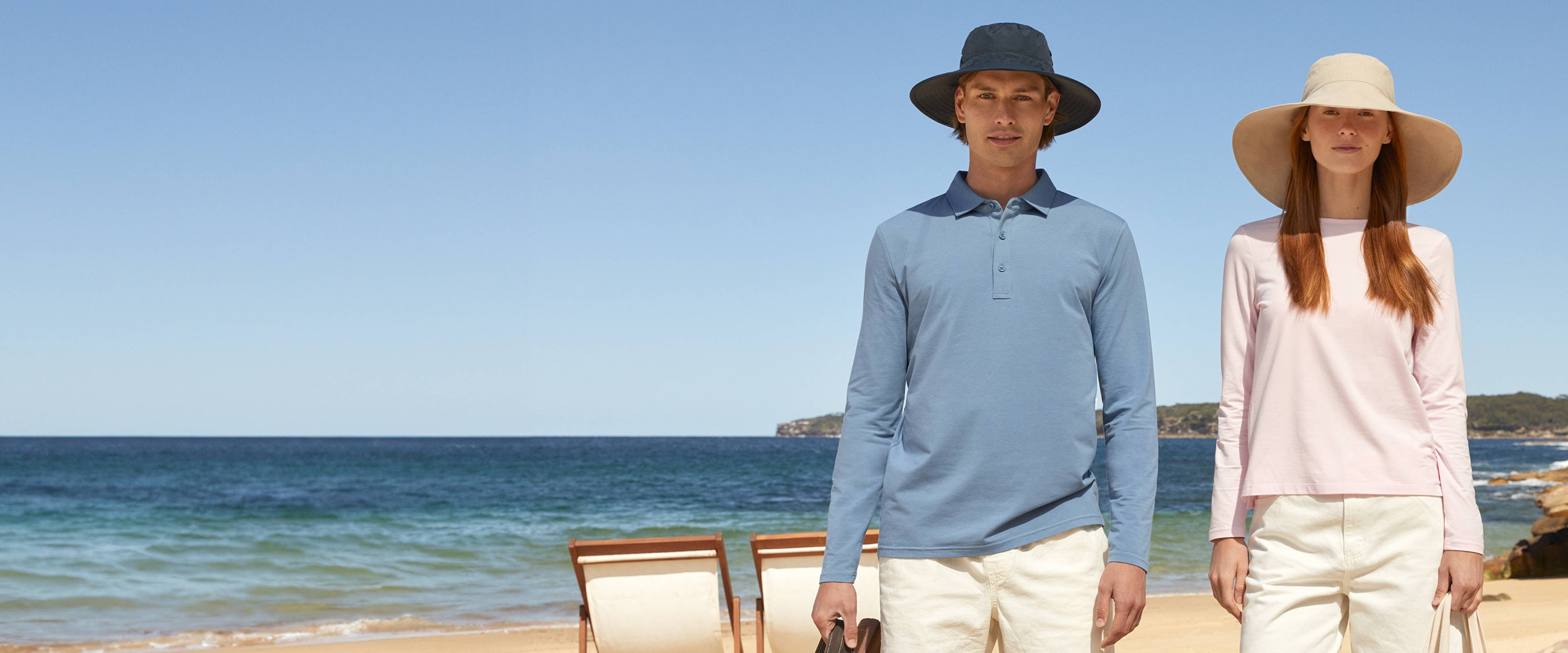 Two people standing on a beach with clear blue sky and ocean.