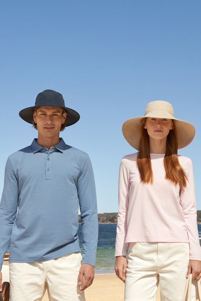 Two people wearing sun hats on a beach with clear blue sky and ocean.
